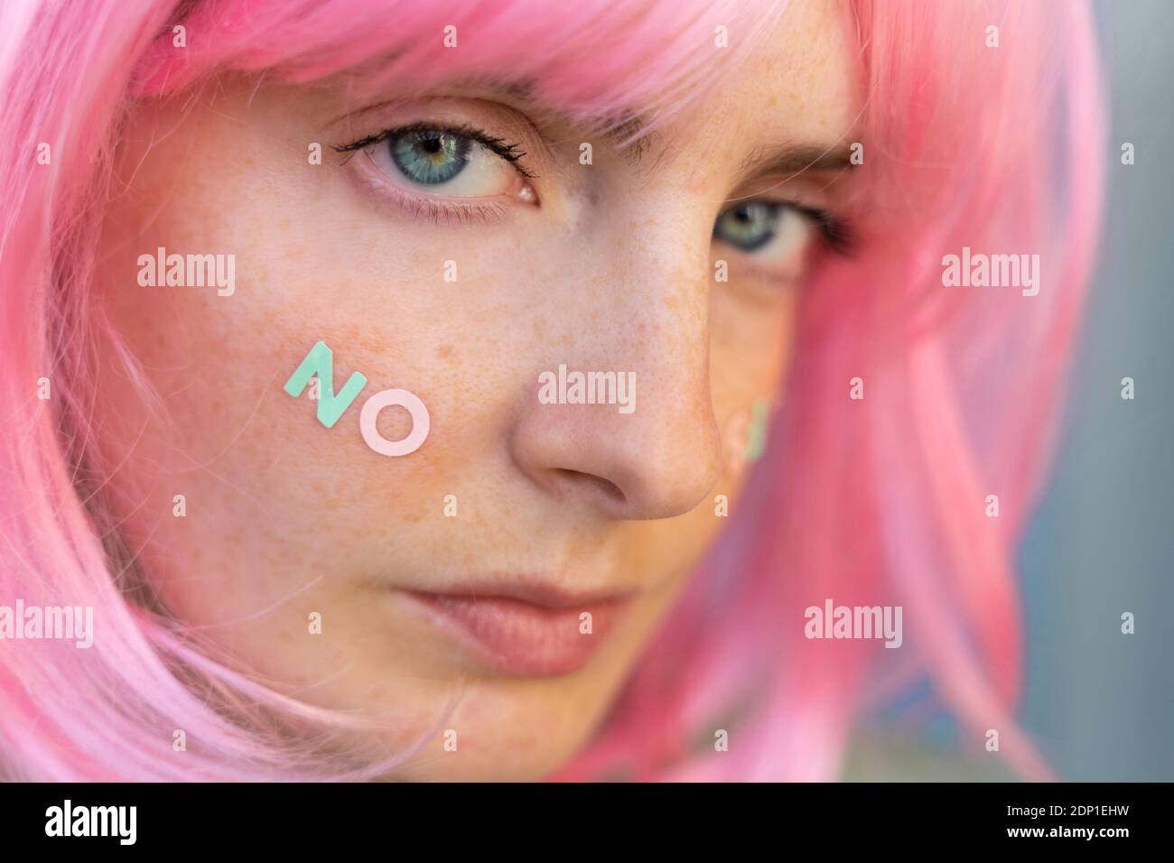 Portrait of young woman wearing pink wig with word 'no' on her cheek Stock Photo