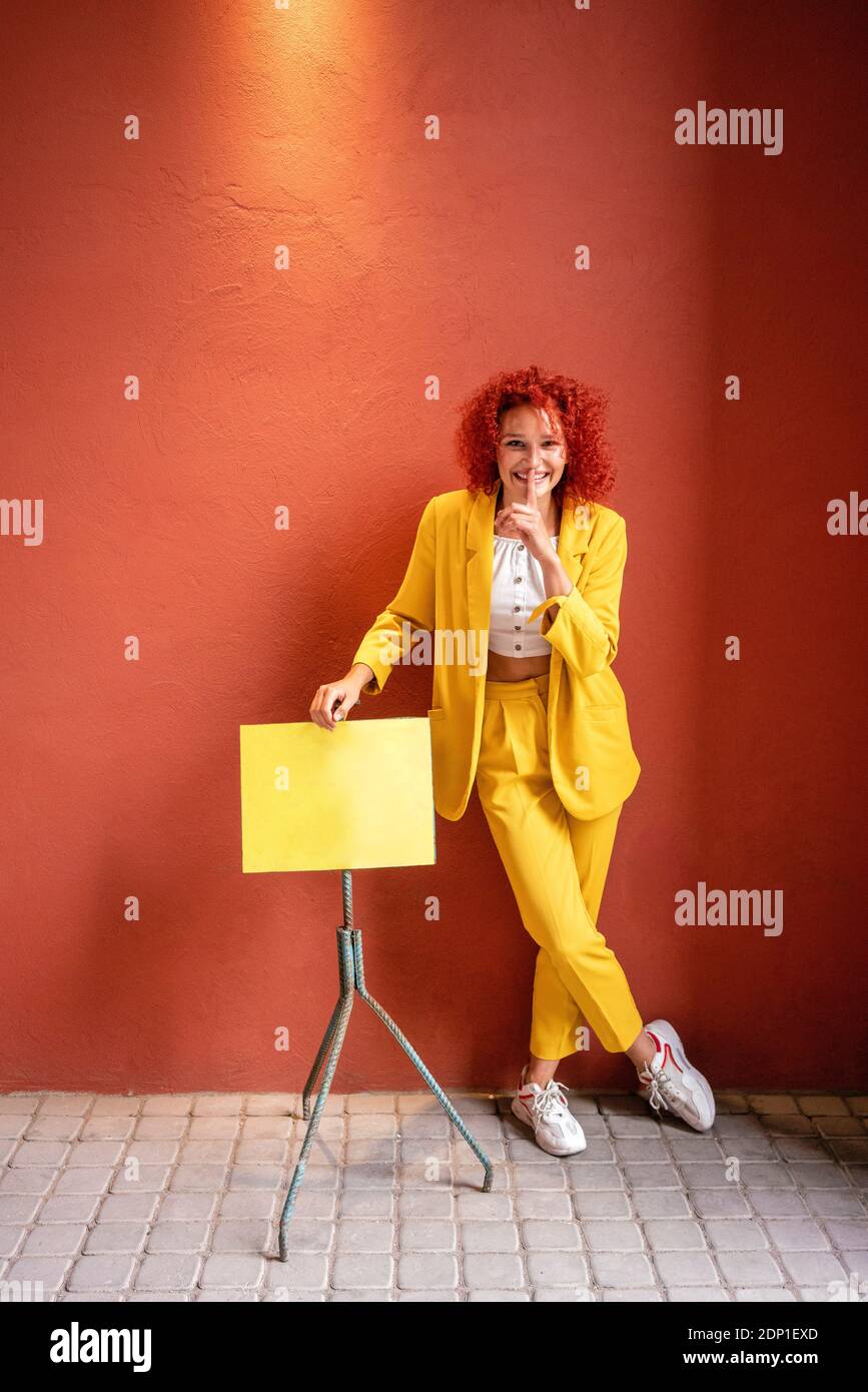 Young woman  in yellow suit leaning on music stand with finger on mouth Stock Photo