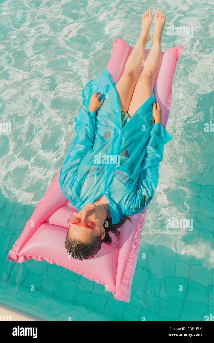 Woman wearing blue rain coat relaxing on pink airbed in swimming