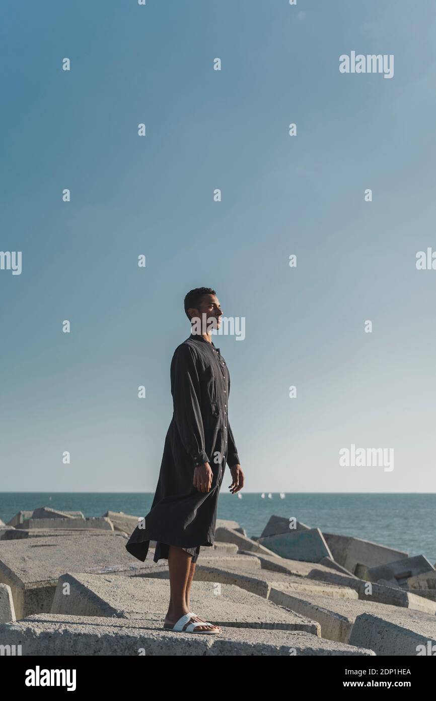 Young man standing at the coast wearing black kaftan Stock Photo