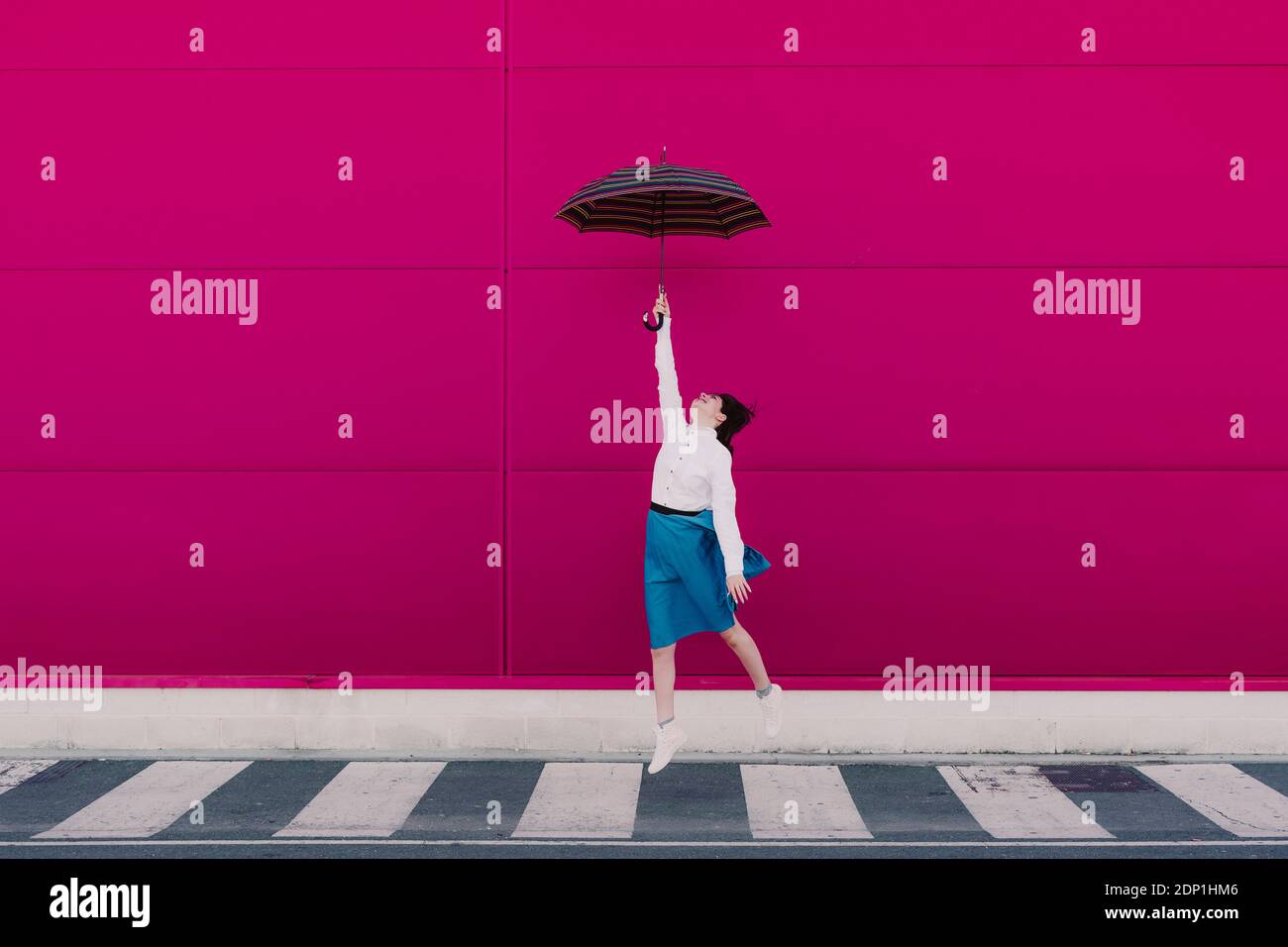 Young woman jumping with umbrella in front of a pink wall Stock Photo ...