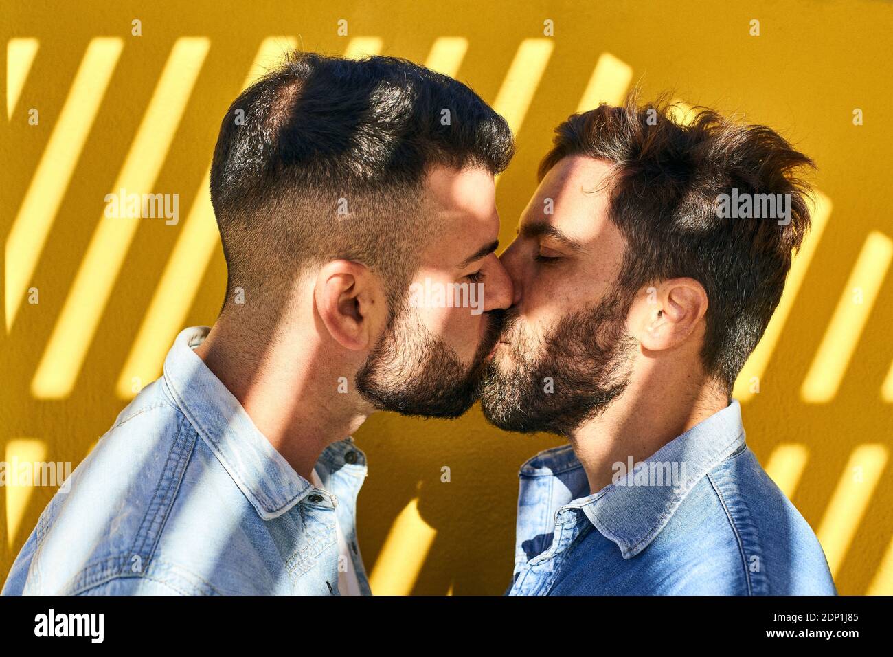 Gay men kissing each other while standing against yellow wall Stock Photo