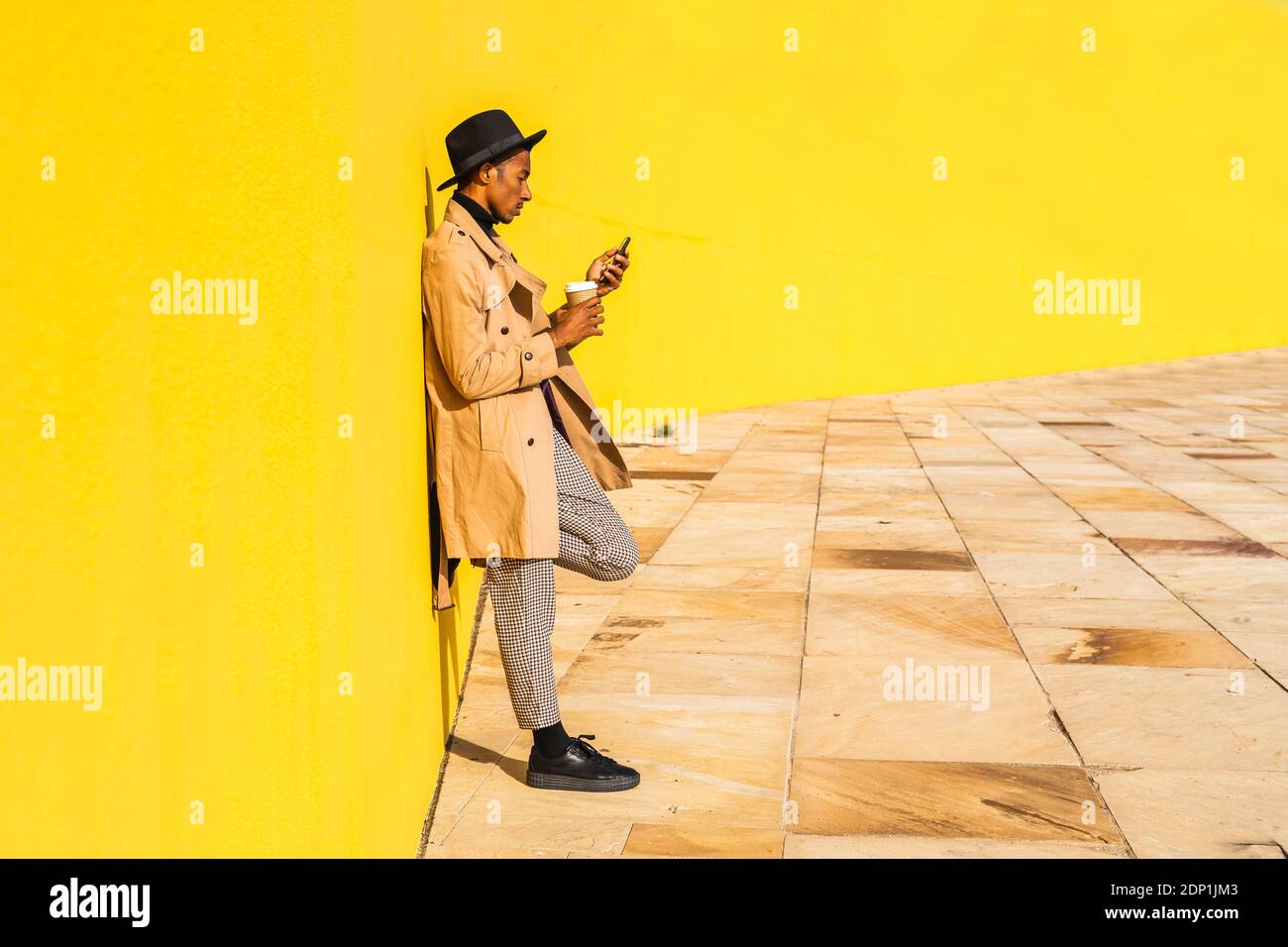 Young man with hat, using smartphone, drinking coffee Stock Photo