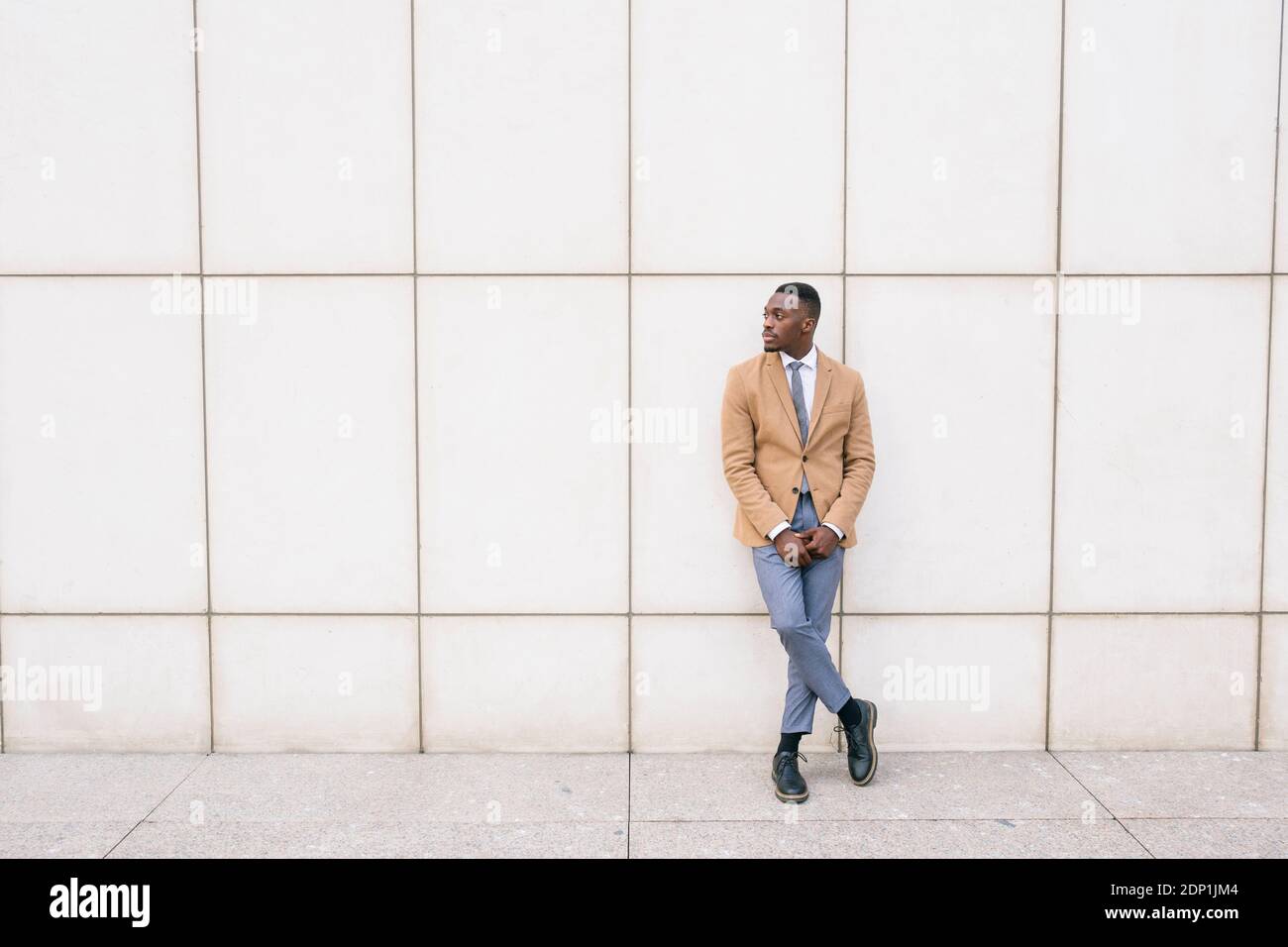 Young businessman leaning against a wall looking sideways Stock Photo