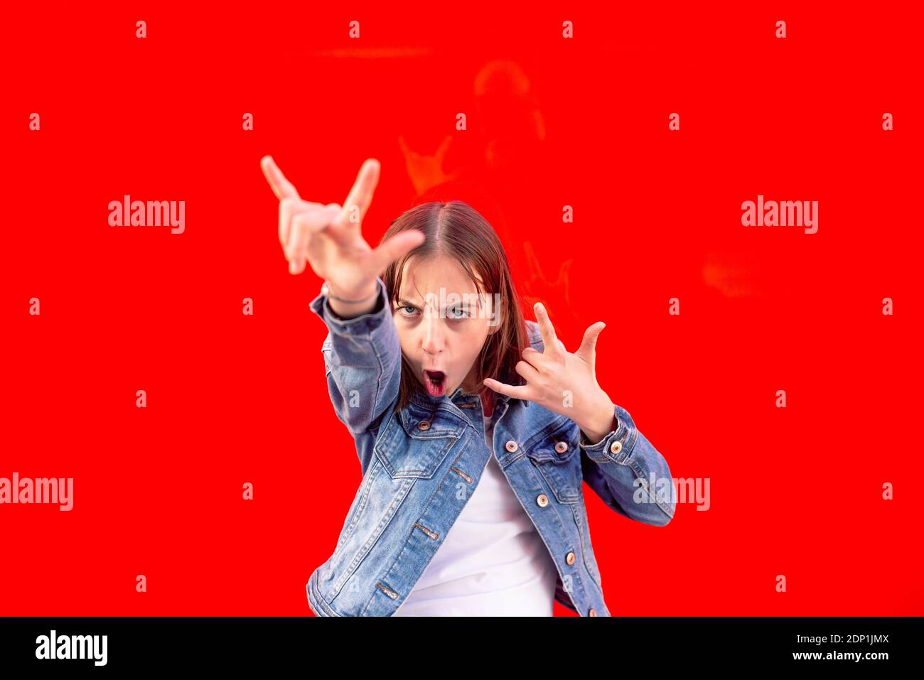 Portrait of teenage girl showing Rock And Roll Sign against red background Stock Photo