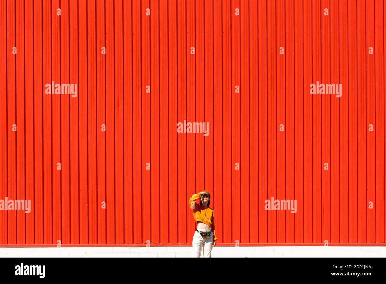 Young woman standing in front of a red wall Stock Photo - Alamy