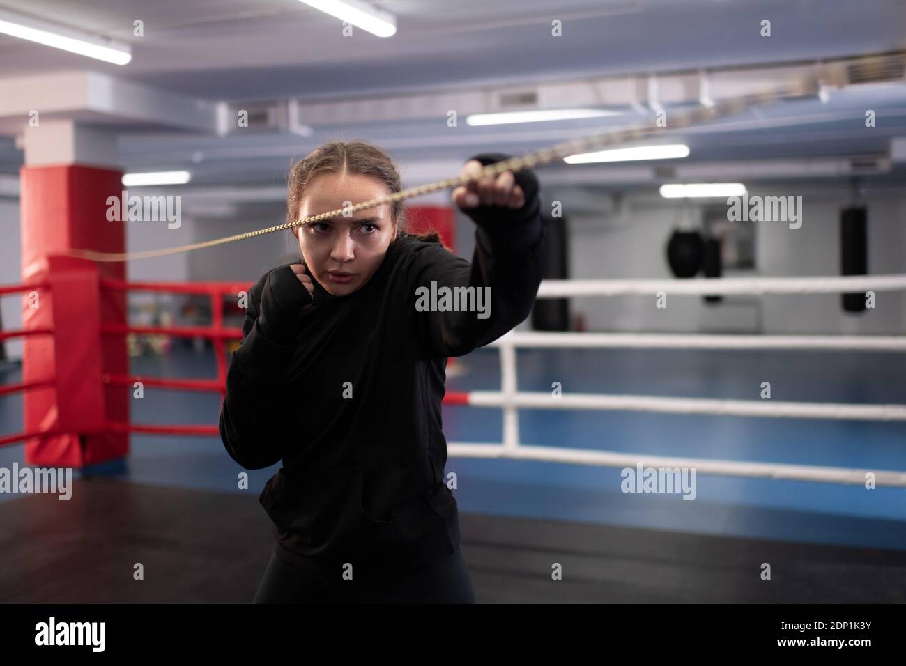 Powerful boxer practicing jabs while standing near rope on boxing ring during training in gym Stock Photo