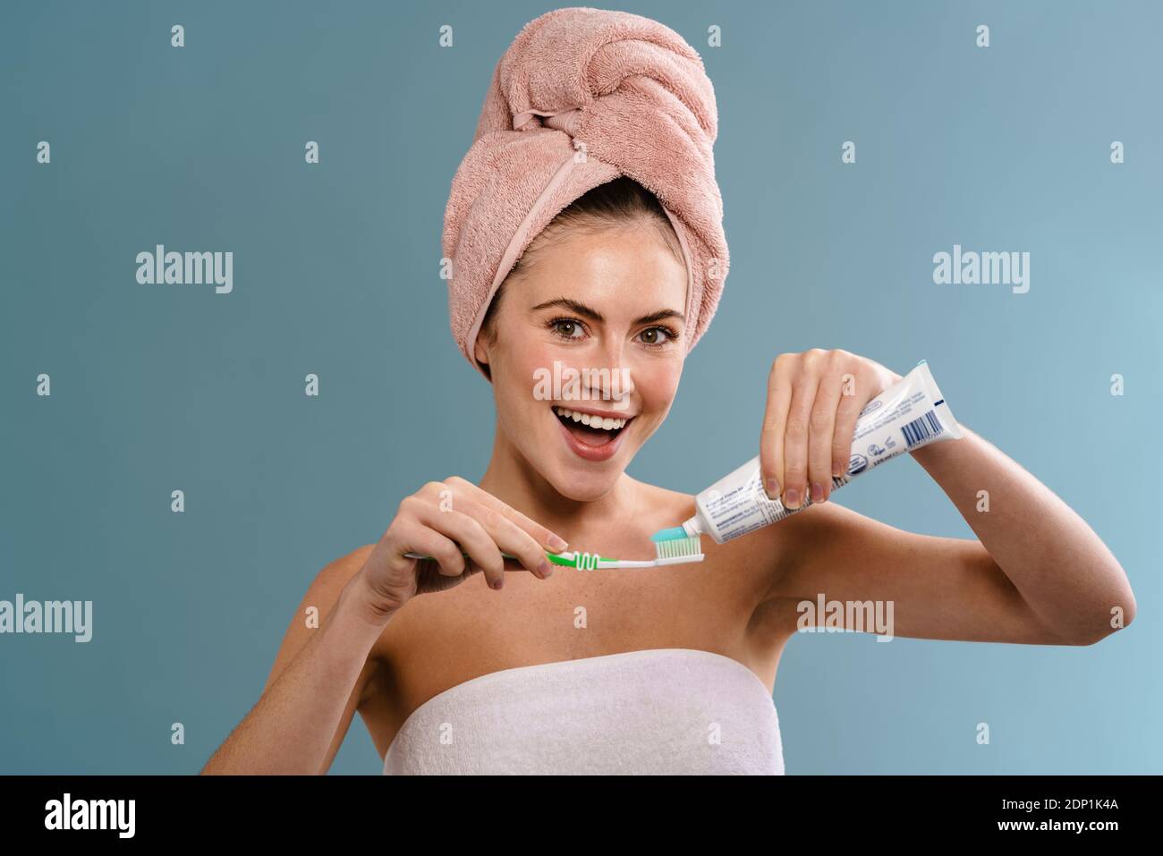 Nice excited girl wearing towels applying toothpaste on toothbrush isolated over blue background Stock Photo