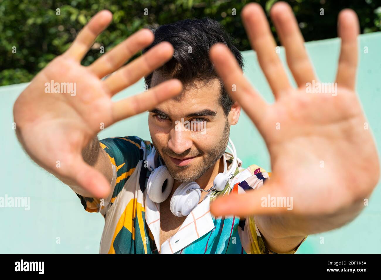 Casual man in front of colorful wall shielding face with his hands ...