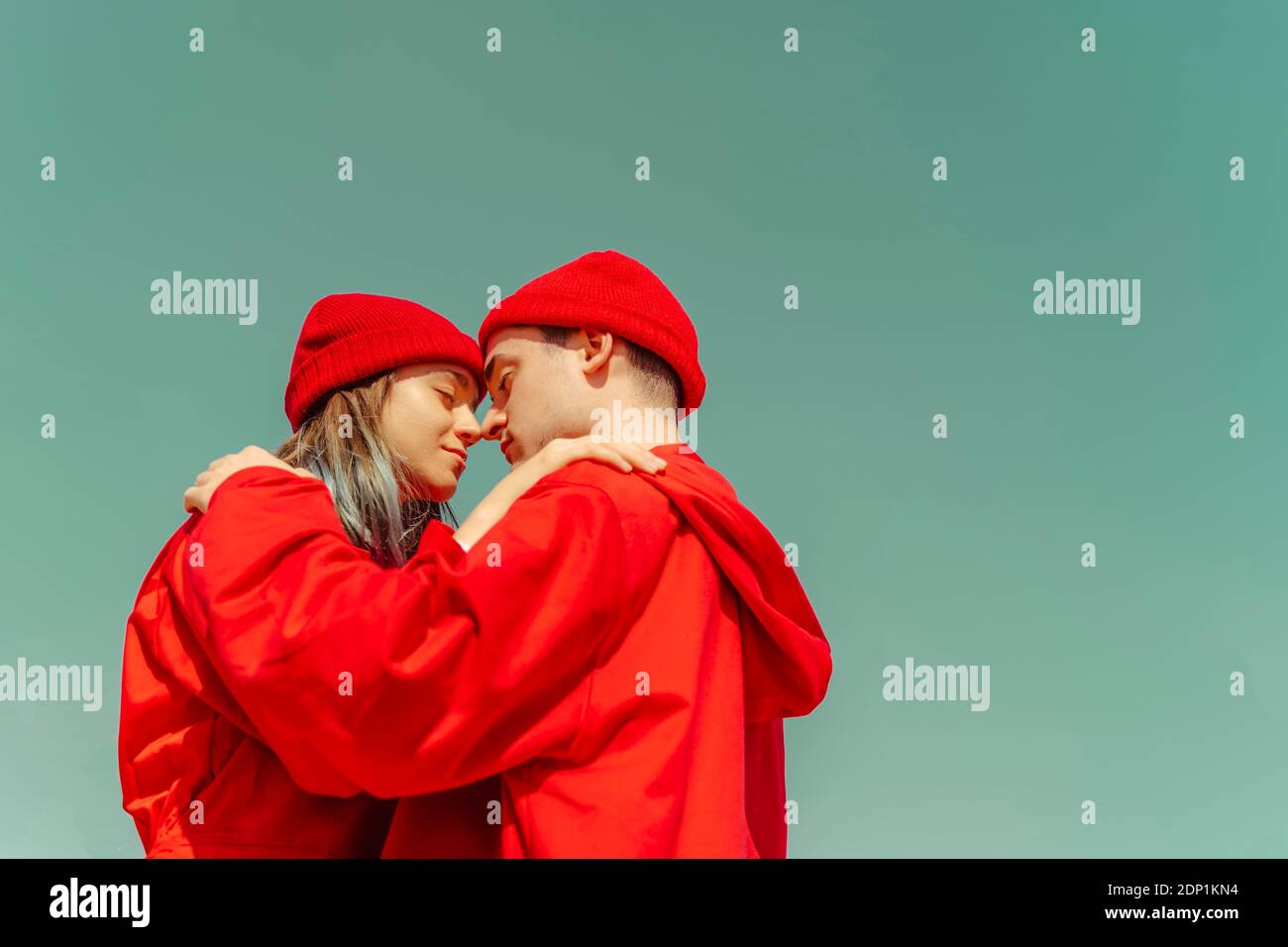 Young couple wearing red overalls and hats standing head to head against sky Stock Photo