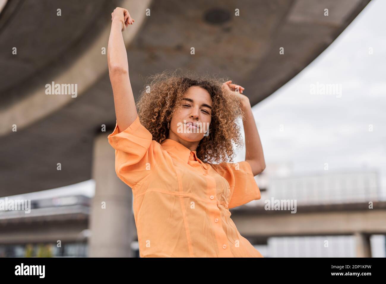 Woman with arms raised and eyes closed dancing while standing outdoors Stock Photo