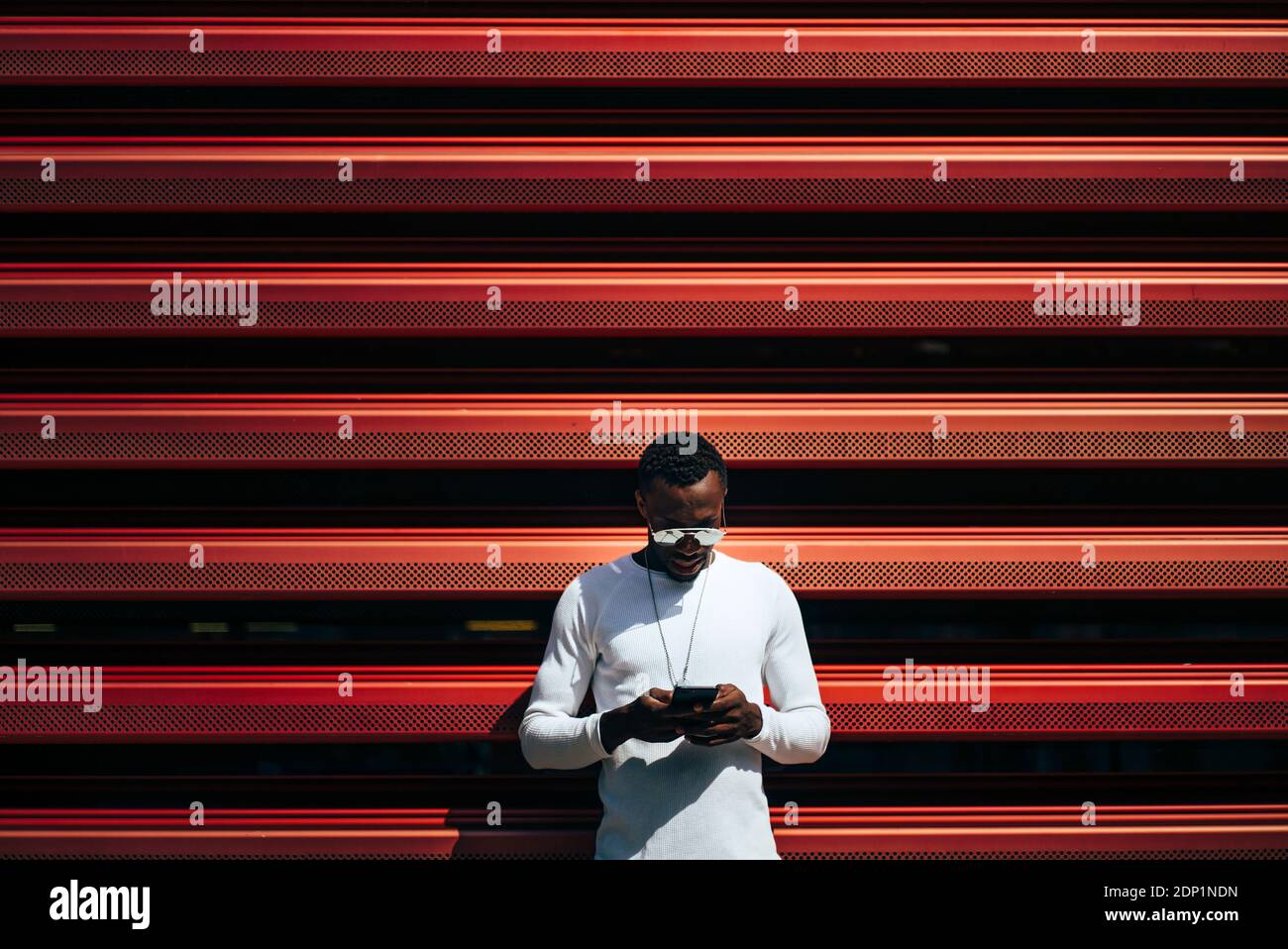 Young man using mobile phone at a red wall Stock Photo
