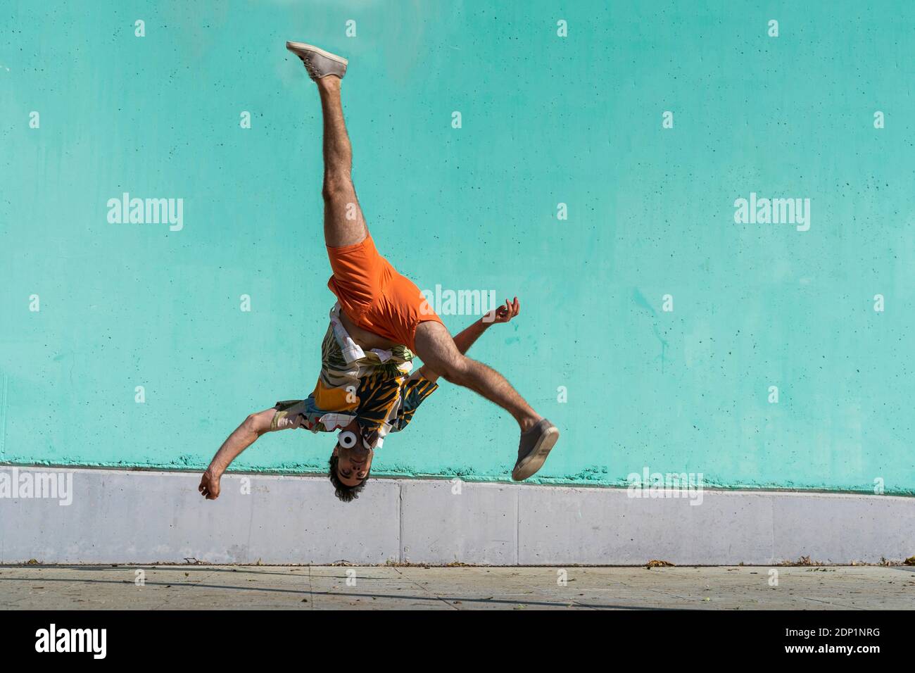 Casual man somersaulting in front of green wall Stock Photo