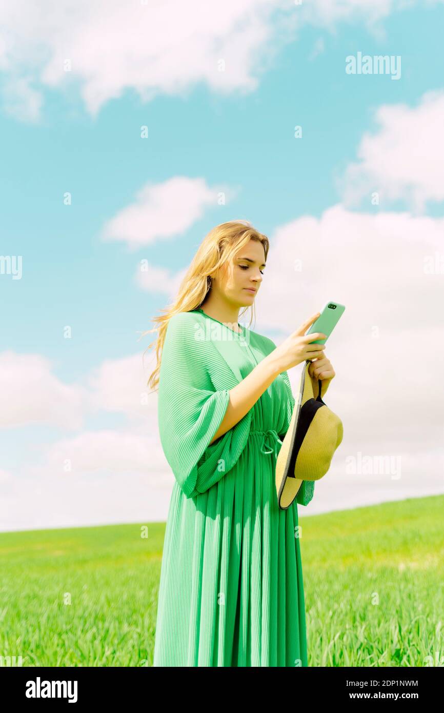 Young woman wearing green dress standing on a field using smartphone ...