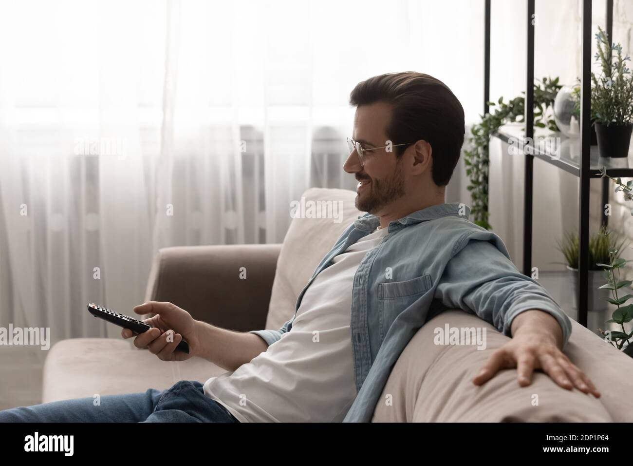 Relaxed young man watching tv choosing channel using remote control Stock Photo
