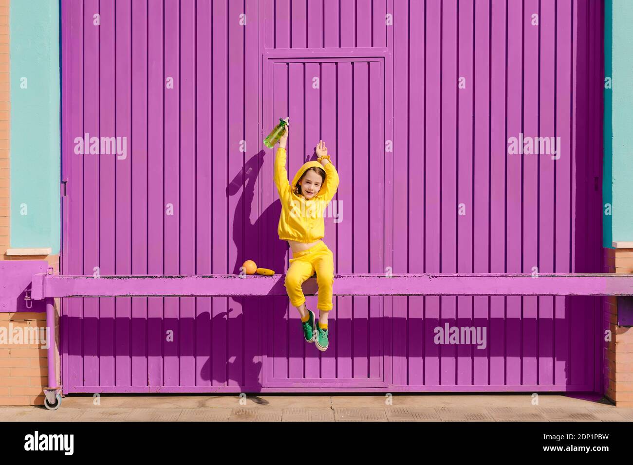 Happy little girl dressed in yellow sitting on bar in front of purple garage door Stock Photo