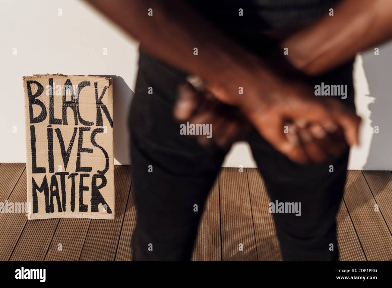 Black Lives Matter sign leaninig on wall, man crossing hands in foreground Stock Photo