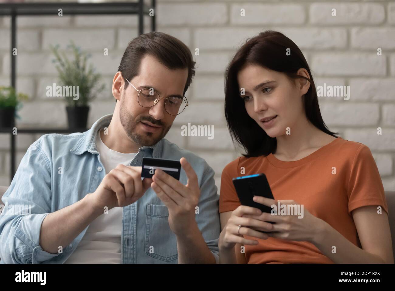Millennial husband teaching wife to make cashless payment using phone Stock Photo