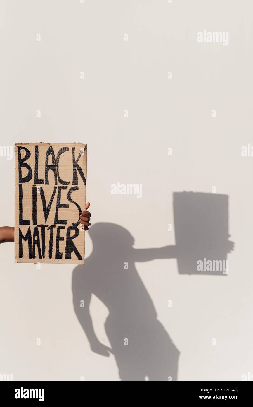 Hand holding Black Lives Matter sign, shadow of person on the wall Stock Photo
