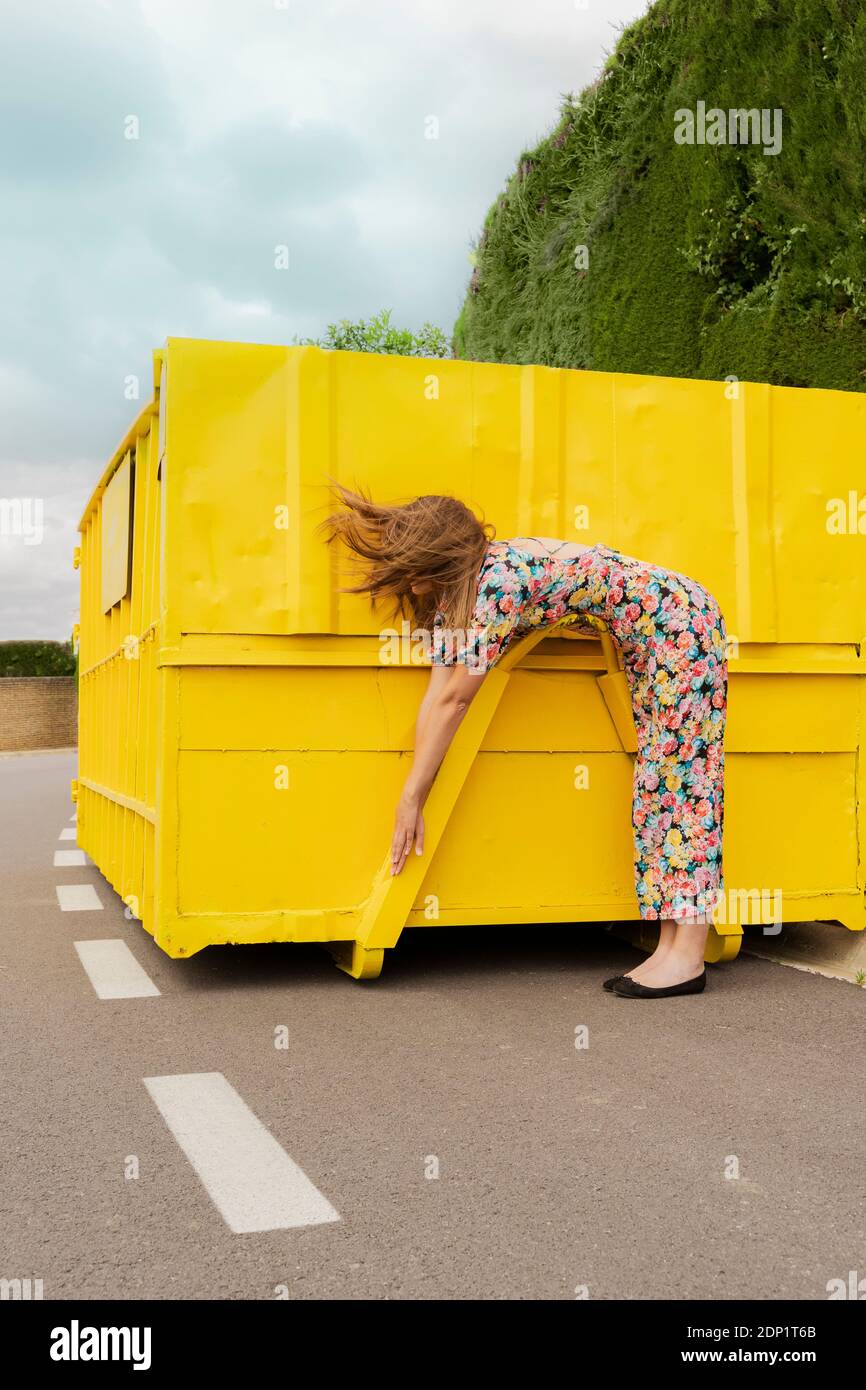 Woman in flower dress bending over attachment of yellow container Stock Photo