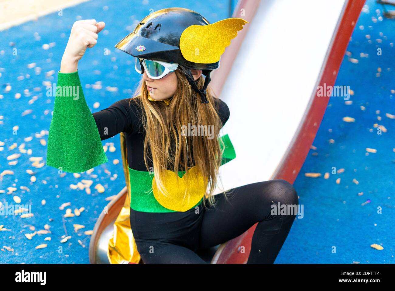 Girl in super heroine costume on playground slide flexing muscles Stock Photo