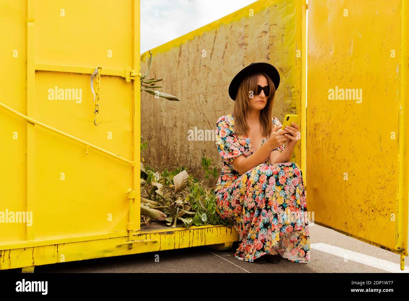 Woman wearing flower dress, sitting in yellow container, using