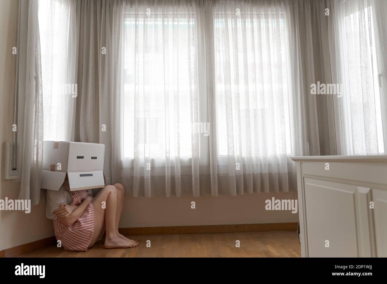 Woman wearing a cardbox on head with bored smiley and cowering on the floor Stock Photo