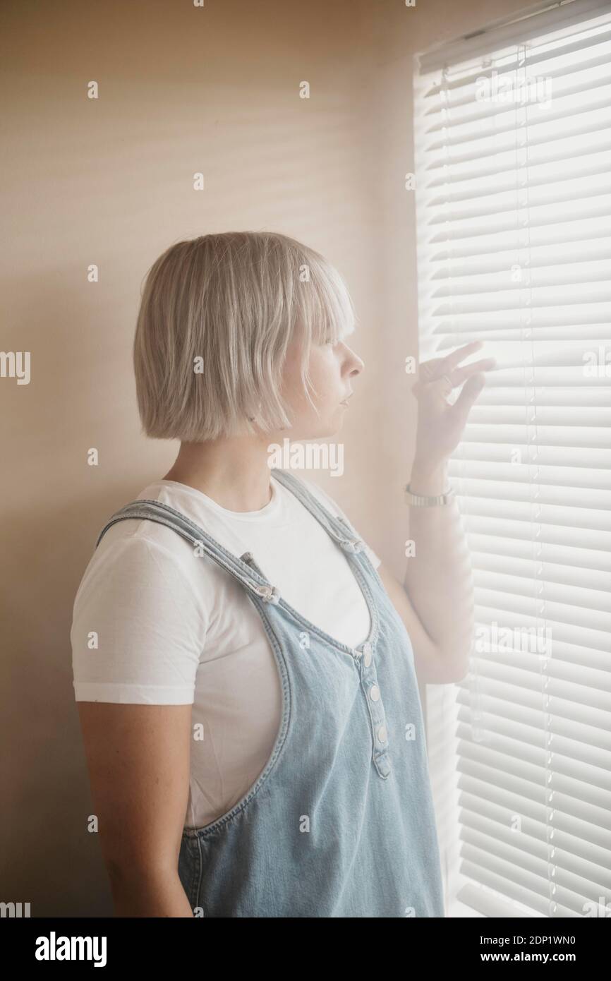 Young woman looking through blinds at the window Stock Photo