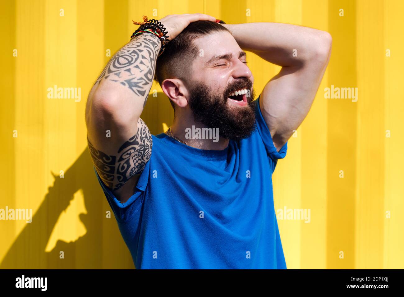 Laughing young man with tattoo standing in front of yellow wall Stock Photo