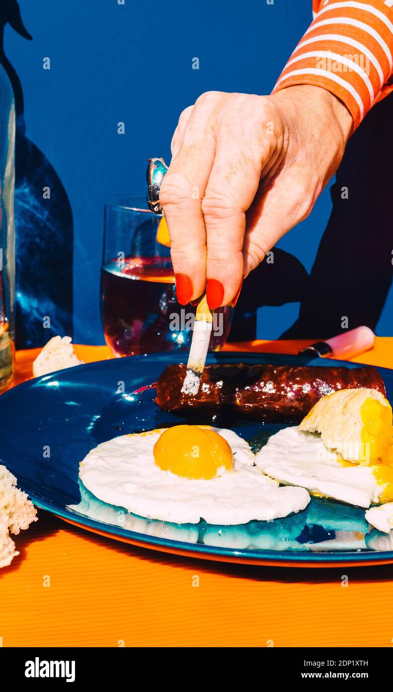 eating eggs like smoking cigarettes Hand of senior woman extinguishing cigarette in fried egg Stock Photo