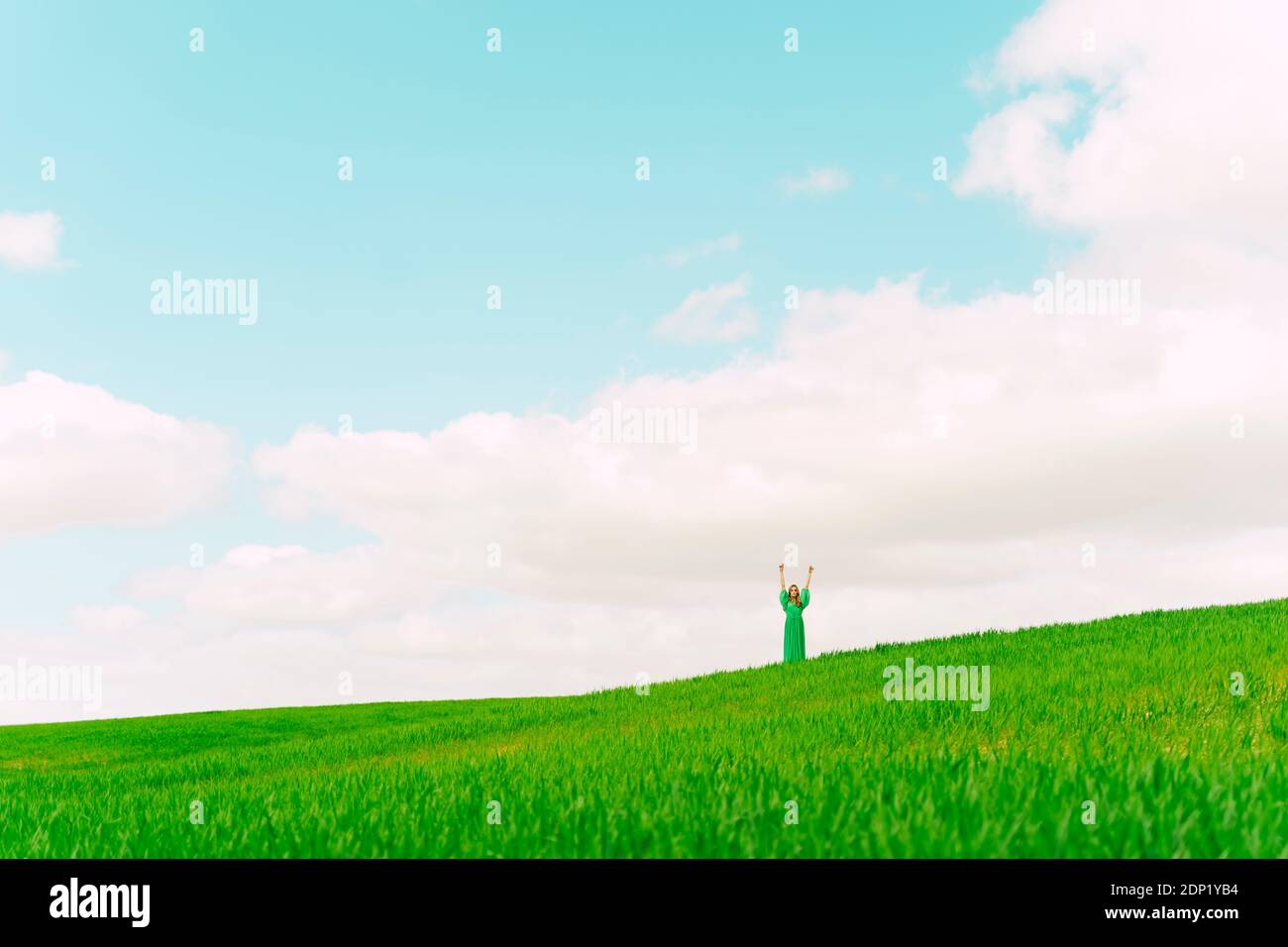Young woman wearing green dress standing on a field with hands raised ...