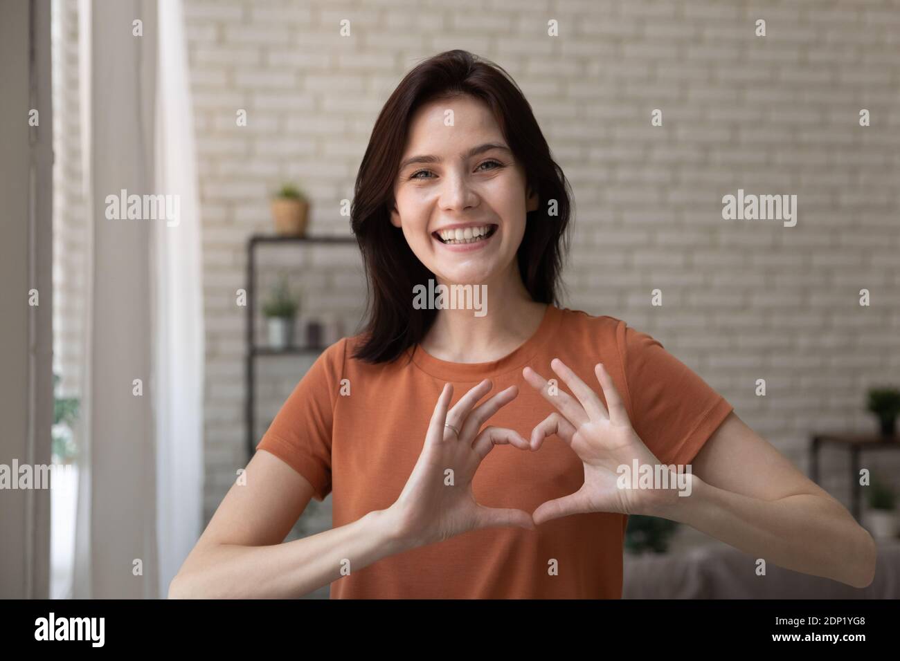 Romantic young lady looking at camera uniting fingers in heart Stock Photo