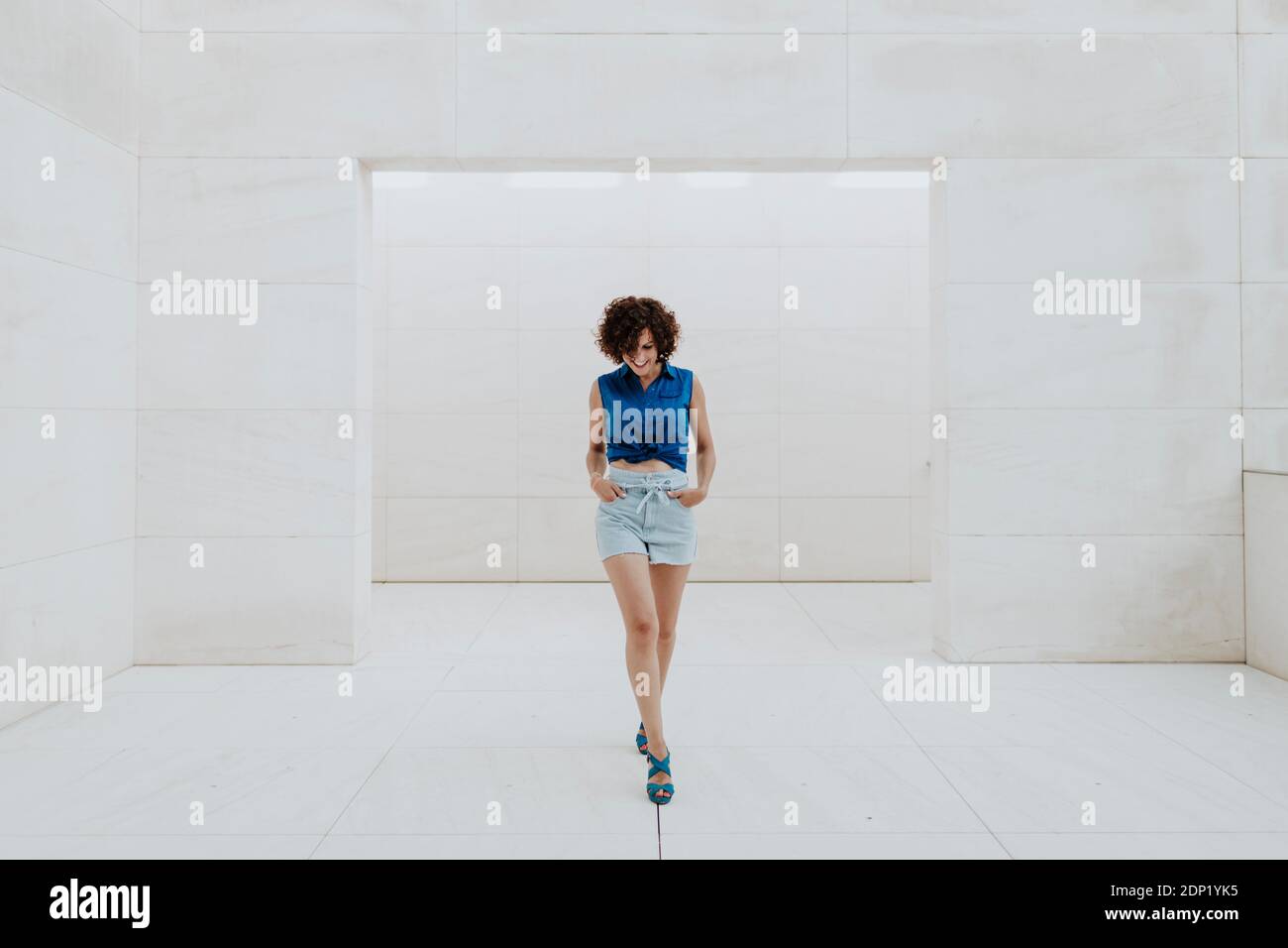 Stylish woman with curly hair walking on tiled floor against wall Stock Photo