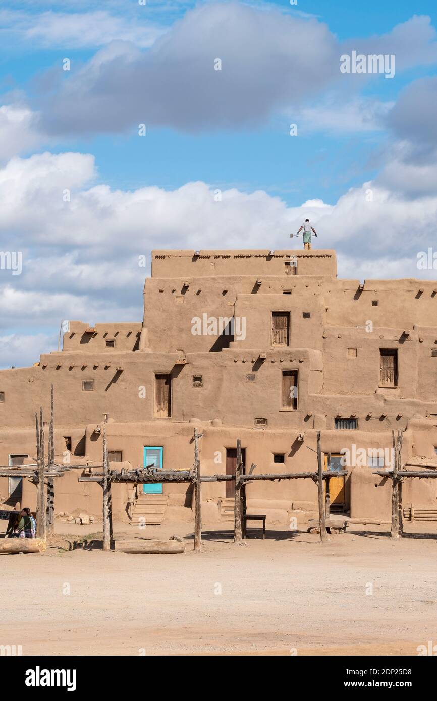 Man cleaning roof of adobe mud brick houses in the historical Native American village of Taos Pueblo, New Mexico, USA. A UNESCO World Heritage Site. Stock Photo