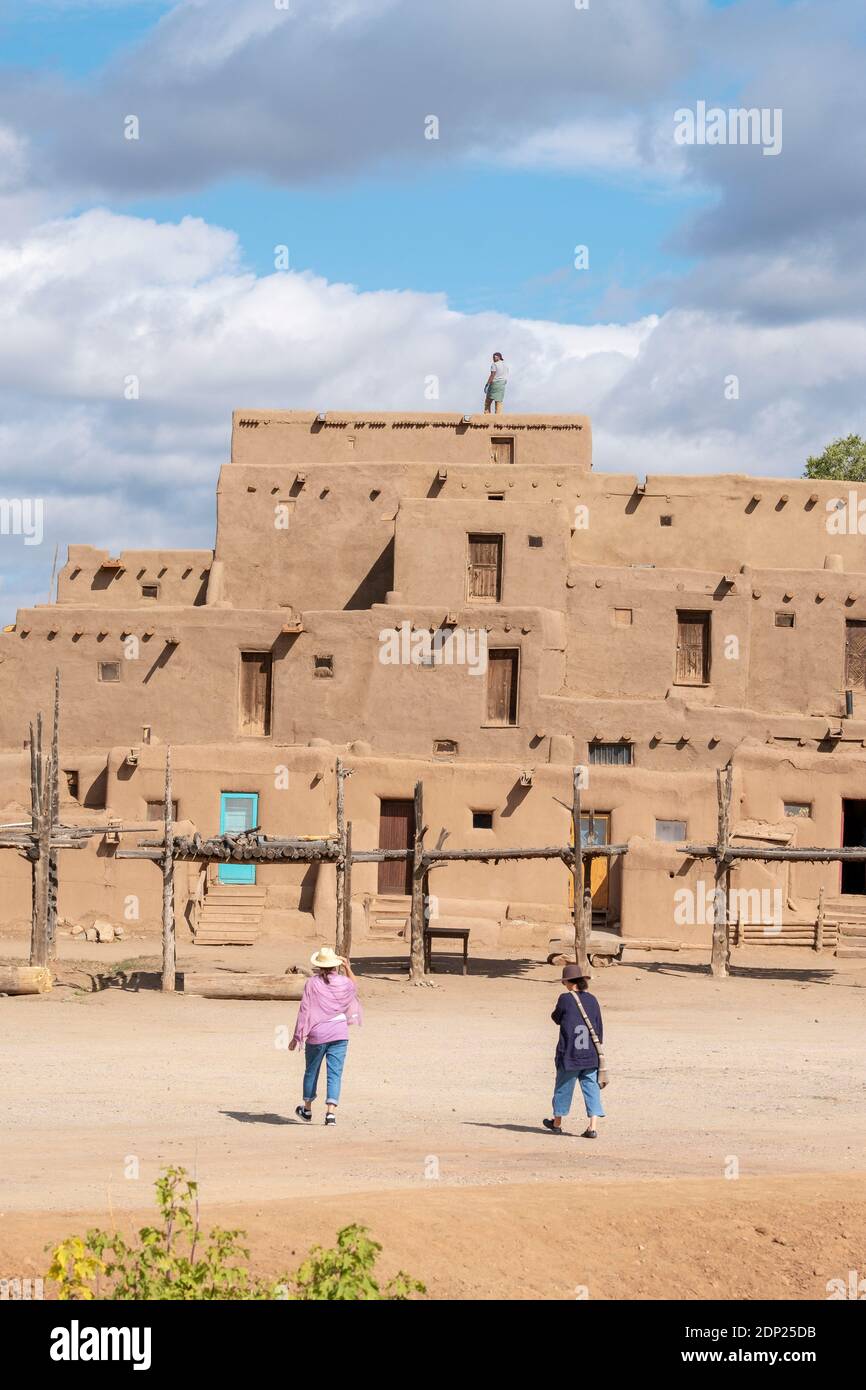 Man cleaning roof of adobe mud brick houses in the historical Native American village of Taos Pueblo, New Mexico, USA. A UNESCO World Heritage Site. Stock Photo