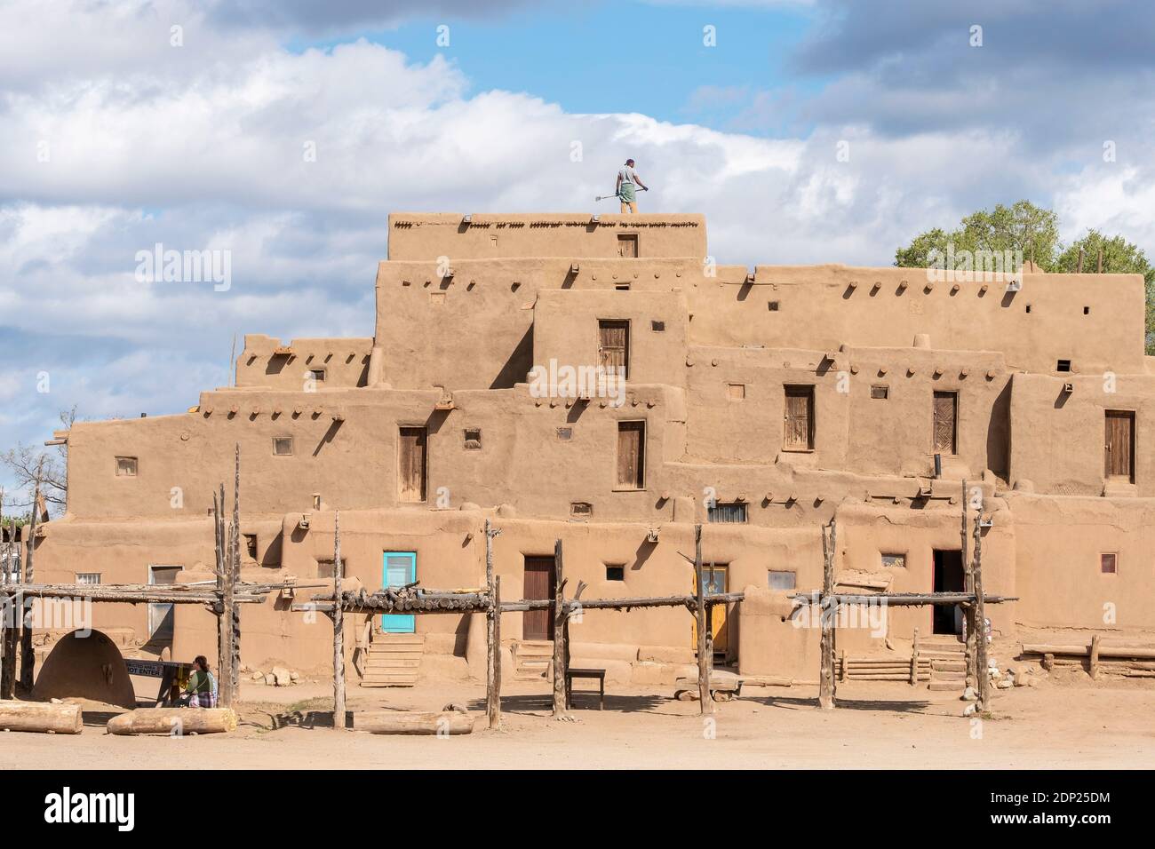 Man cleaning roof of adobe mud brick houses in the historical Native American village of Taos Pueblo, New Mexico, USA. A UNESCO World Heritage Site. Stock Photo
