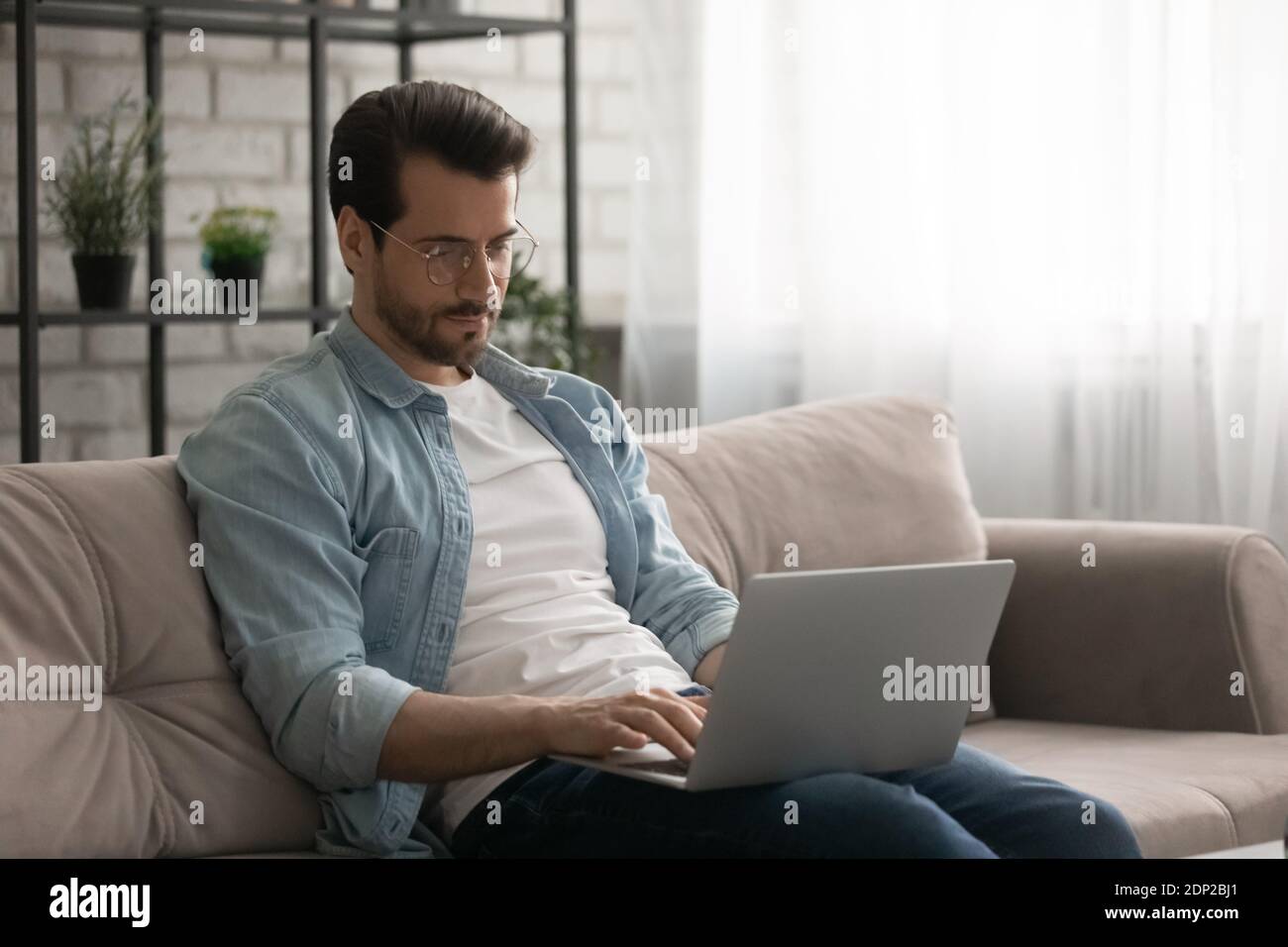 Confident young man sitting on sofa at home using laptop Stock Photo