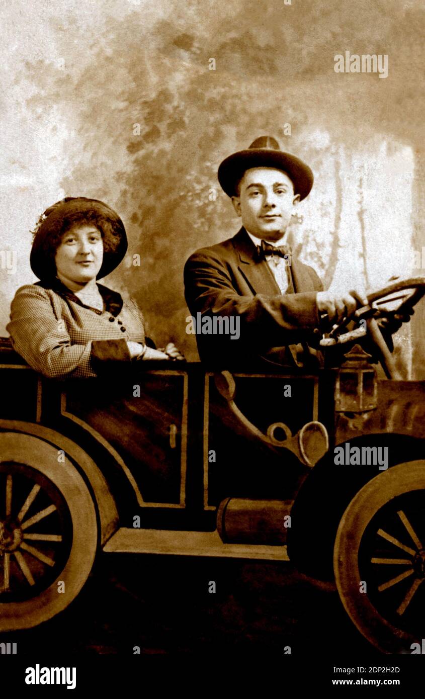 Antique photograph of a couple circa 1920 sitting in a photo studio by a paper automobile. Stock Photo