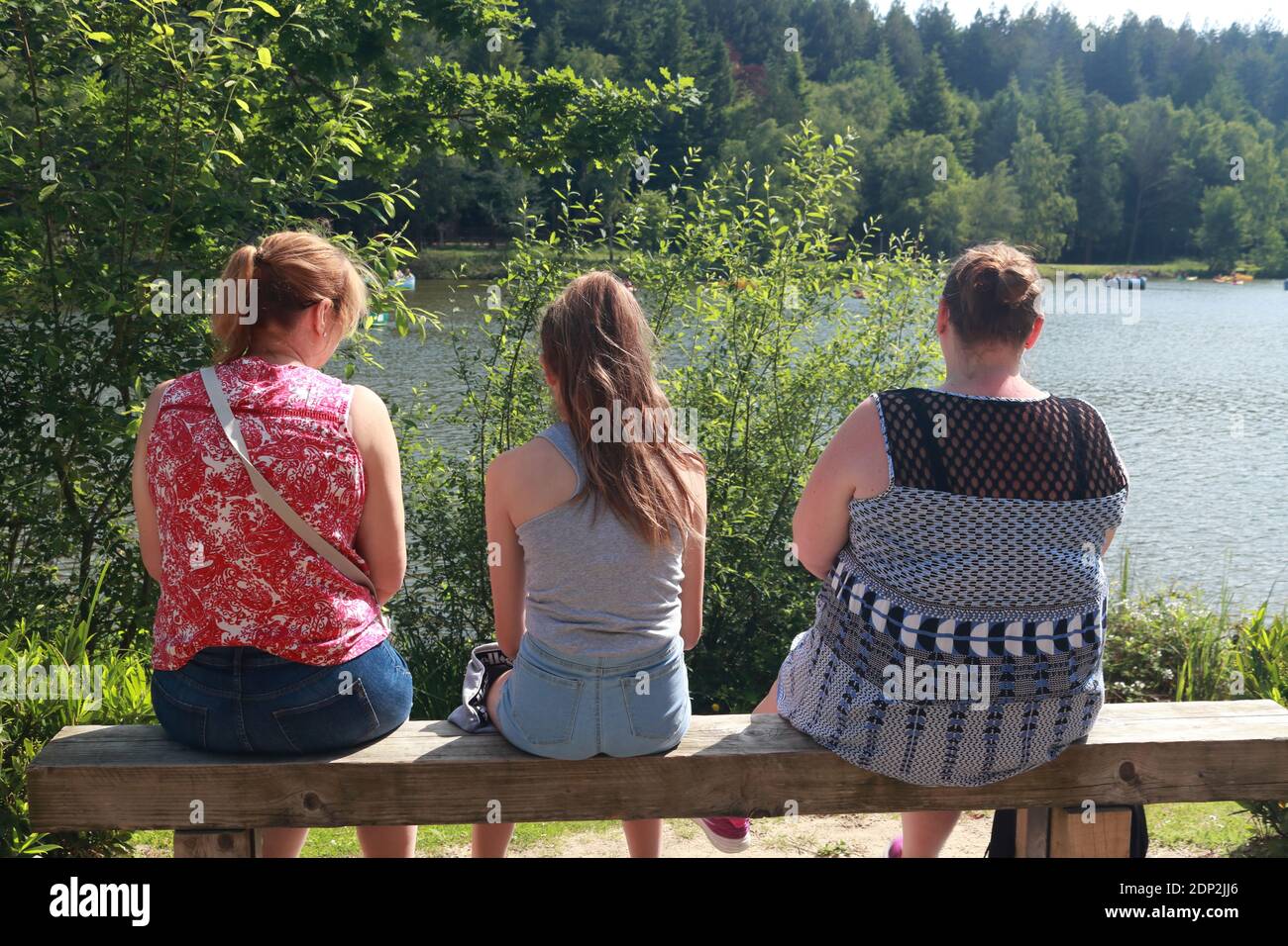 3 generations woman sitting with the backs to camera looking out over a peaceful lake. Stock Photo