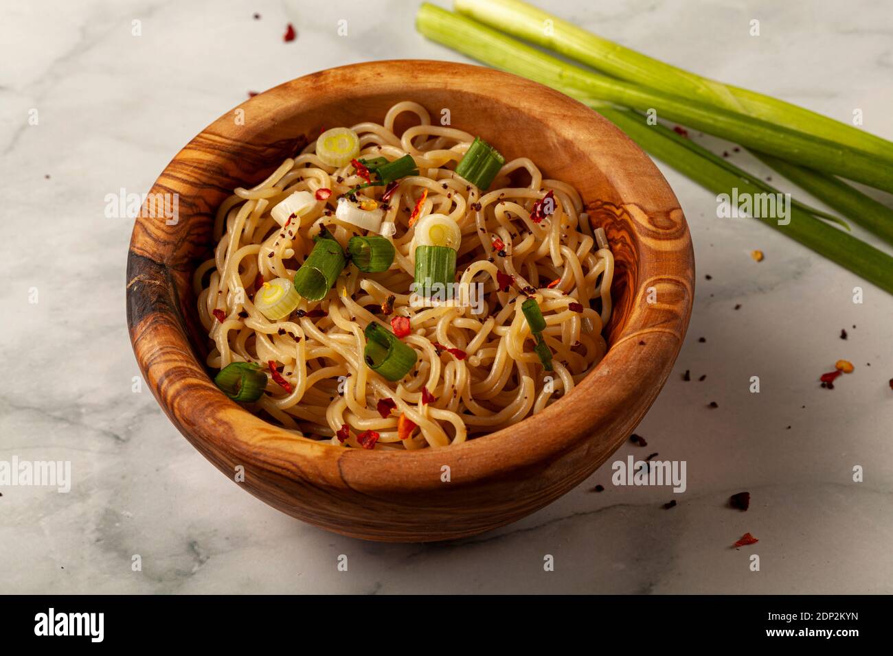 close up image of a wooden bowl full of cooked ramen noodles seasoned with herbs and spices as well as pieces of chopped spring onion. Herbs and peppe Stock Photo