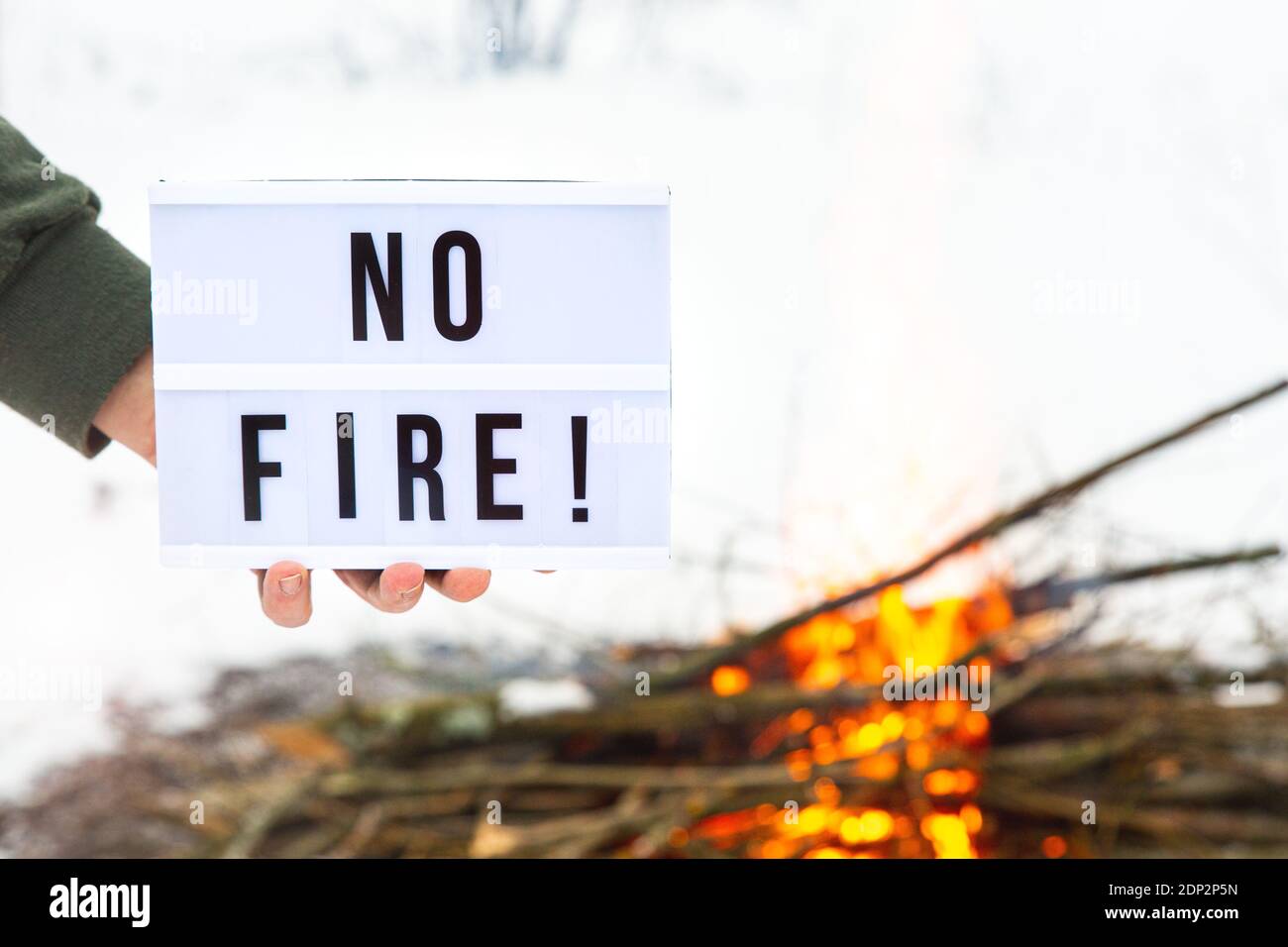 The concept of nature protection, protection from forest fires, ecology. A sign with the text no fire in a man's hand over a flaming bonfire. Stock Photo