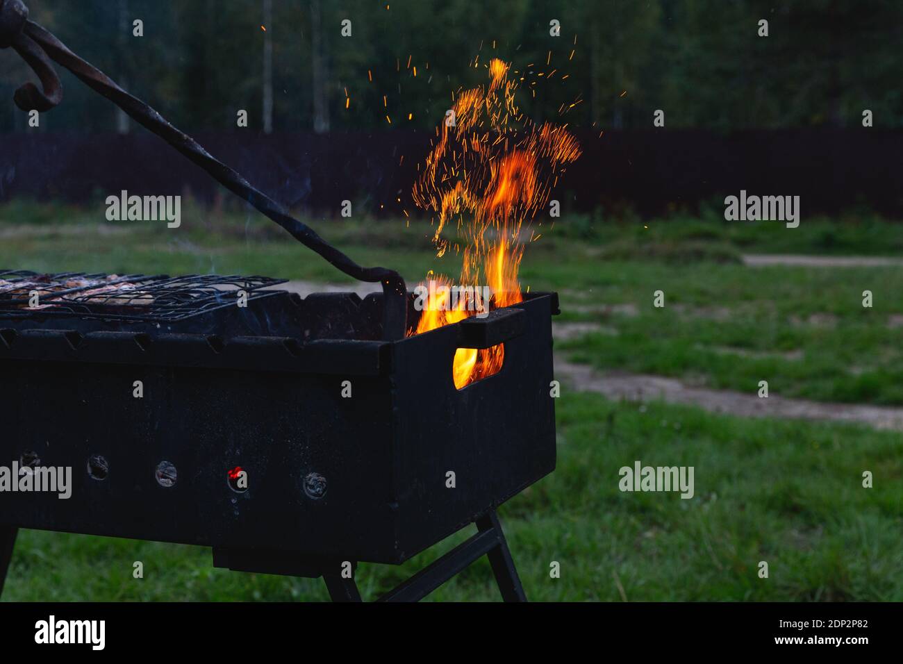 The meat is grilled. A man stirring coals with a hot poker. Sparks fly from the fire in the grill. Outdoor cooking. Meeting with friends, picnic Stock Photo
