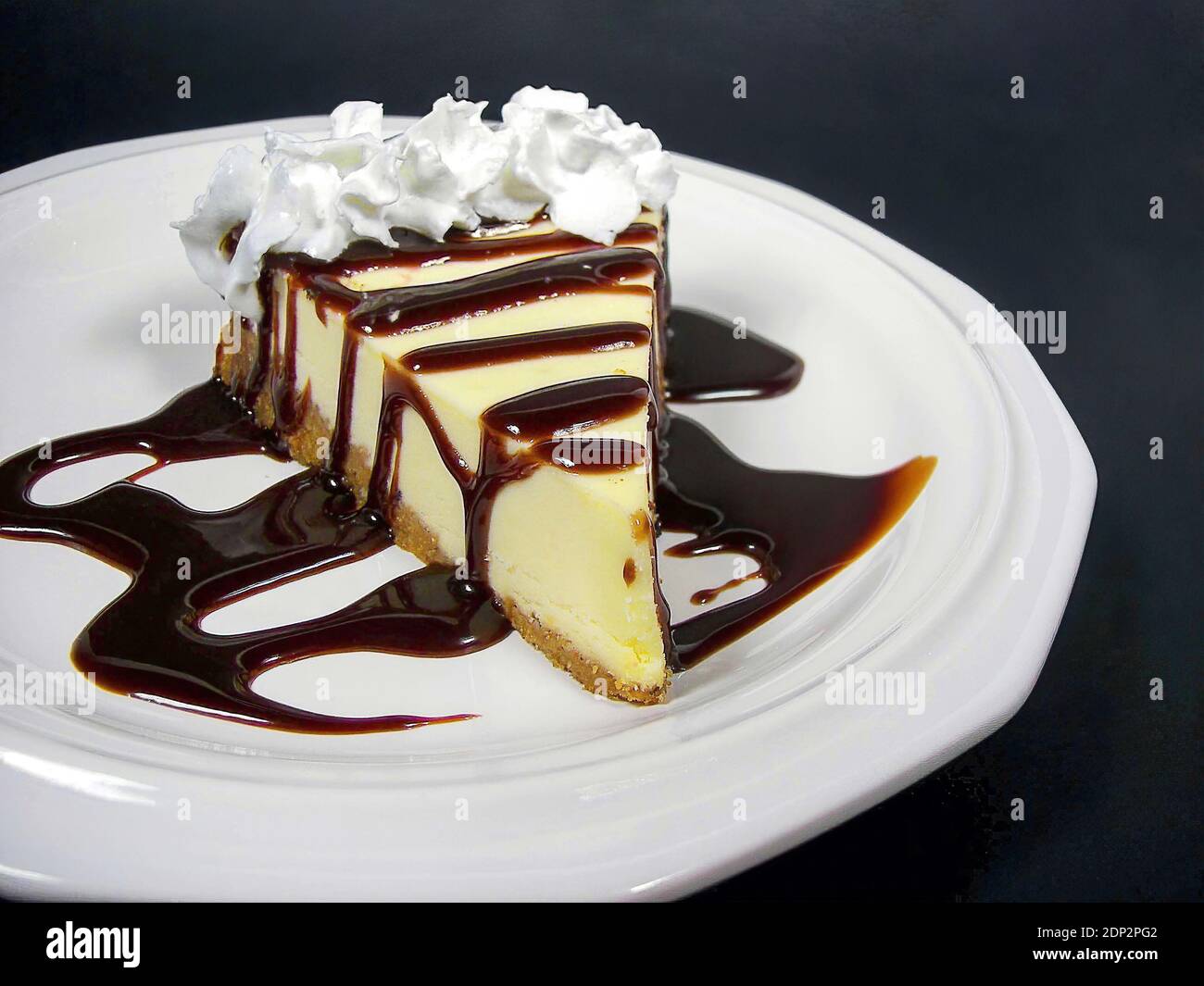 cheesecake slice with chocolate drizzle and whipped cream on white plate isolated on black Stock Photo