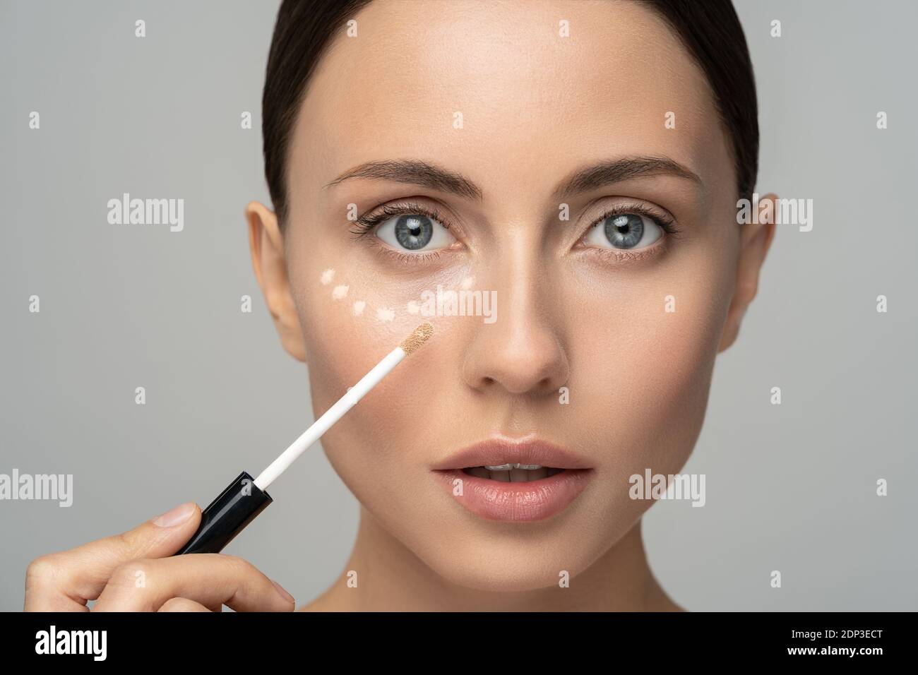 Close up of woman with natural makeup applying corrector on flawless fresh skin, doing make up. Girl after shower put concealer under eye area. Beauty Stock Photo