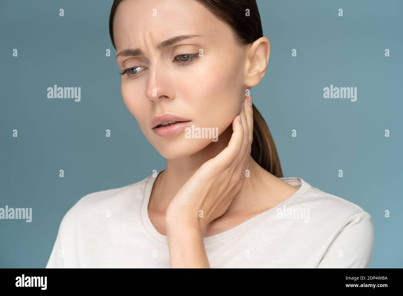 Closeup of sick sad woman checking lymph nodes, caught cold, suffering from throat problems, isolated on studio blue background Stock Photo