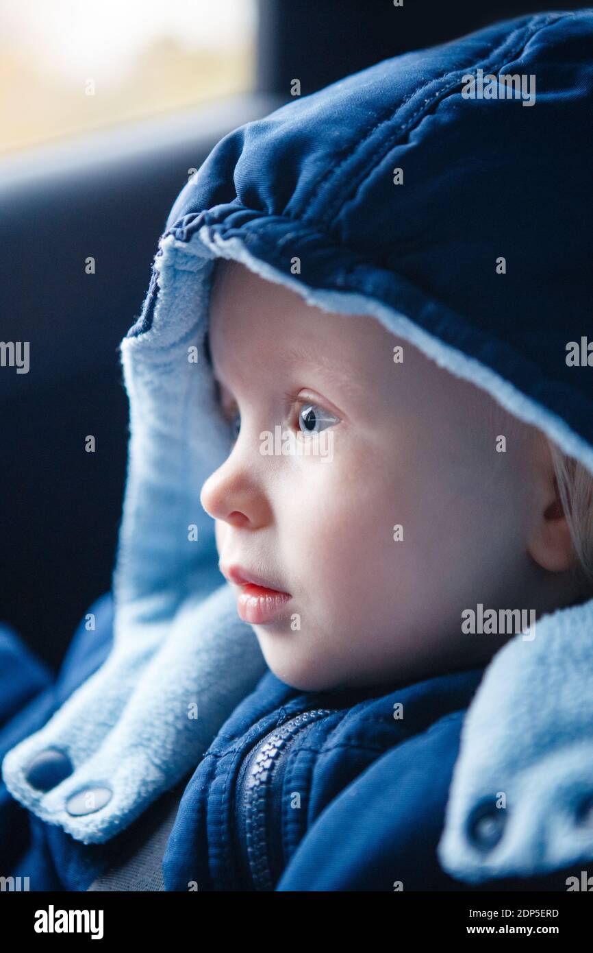 Cute Caucasian baby infant sitting in car seat. Adorable kid in outwear clothes in automobile vehicle carsit fastened with seatbelt. Care, safety and Stock Photo