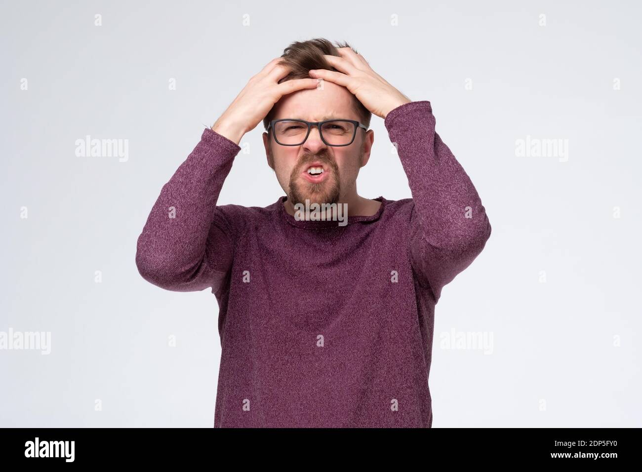 Mature caucasian man with glasses in pain and despair holding hands on head. Studio shot Stock Photo
