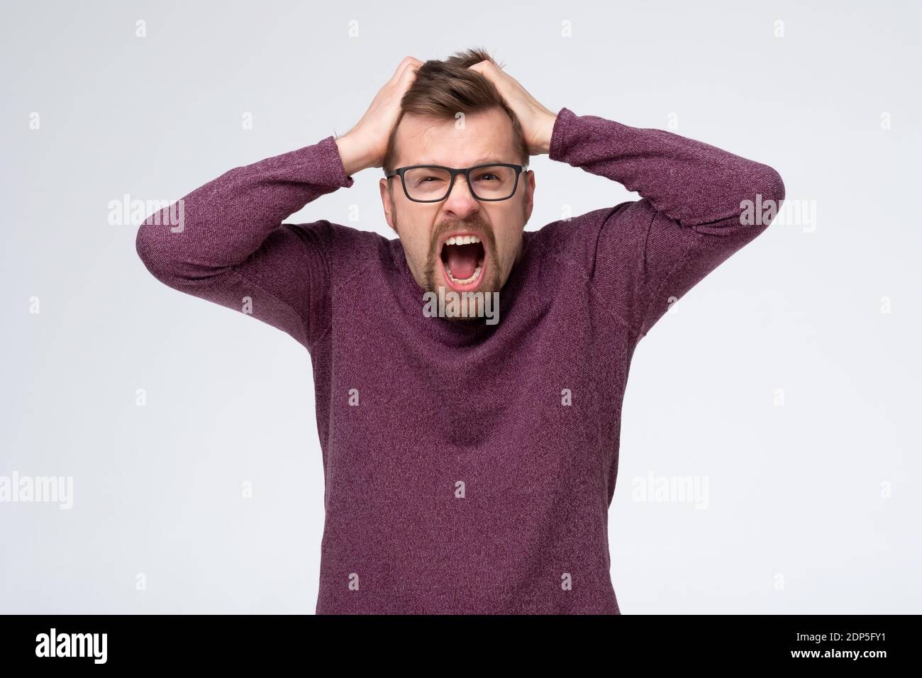 Mature caucasian man with glasses in pain and despair holding hands on head. Studio shot Stock Photo