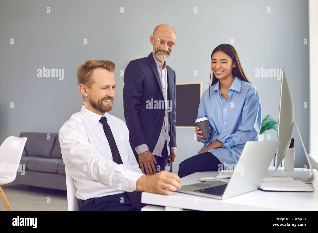 Employees discuss work moments in front of a laptop in a friendly atmosphere smiling and laughing. Stock Photo