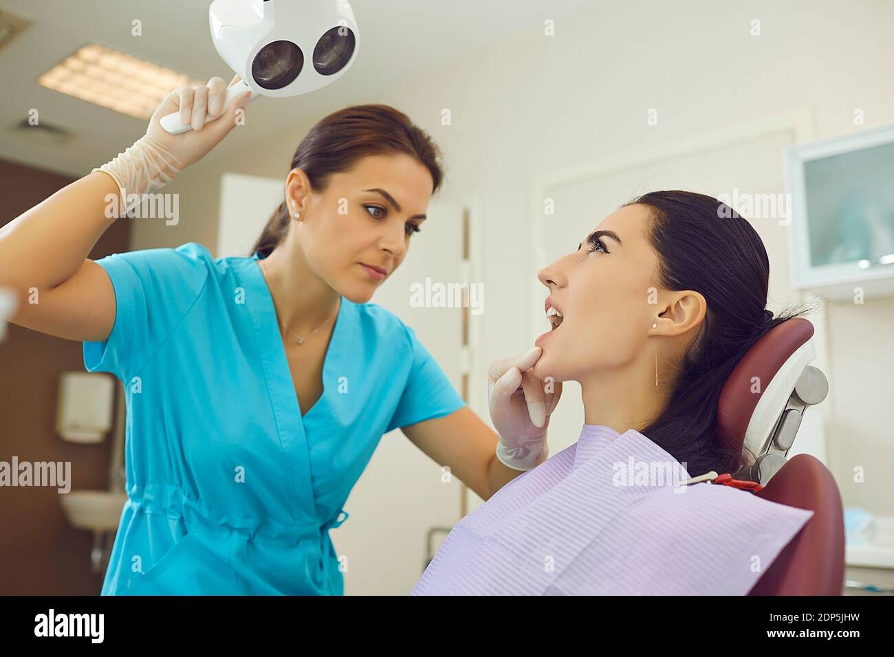 Dentist in medical uniform directing light to woman patients mouth for examination Stock Photo